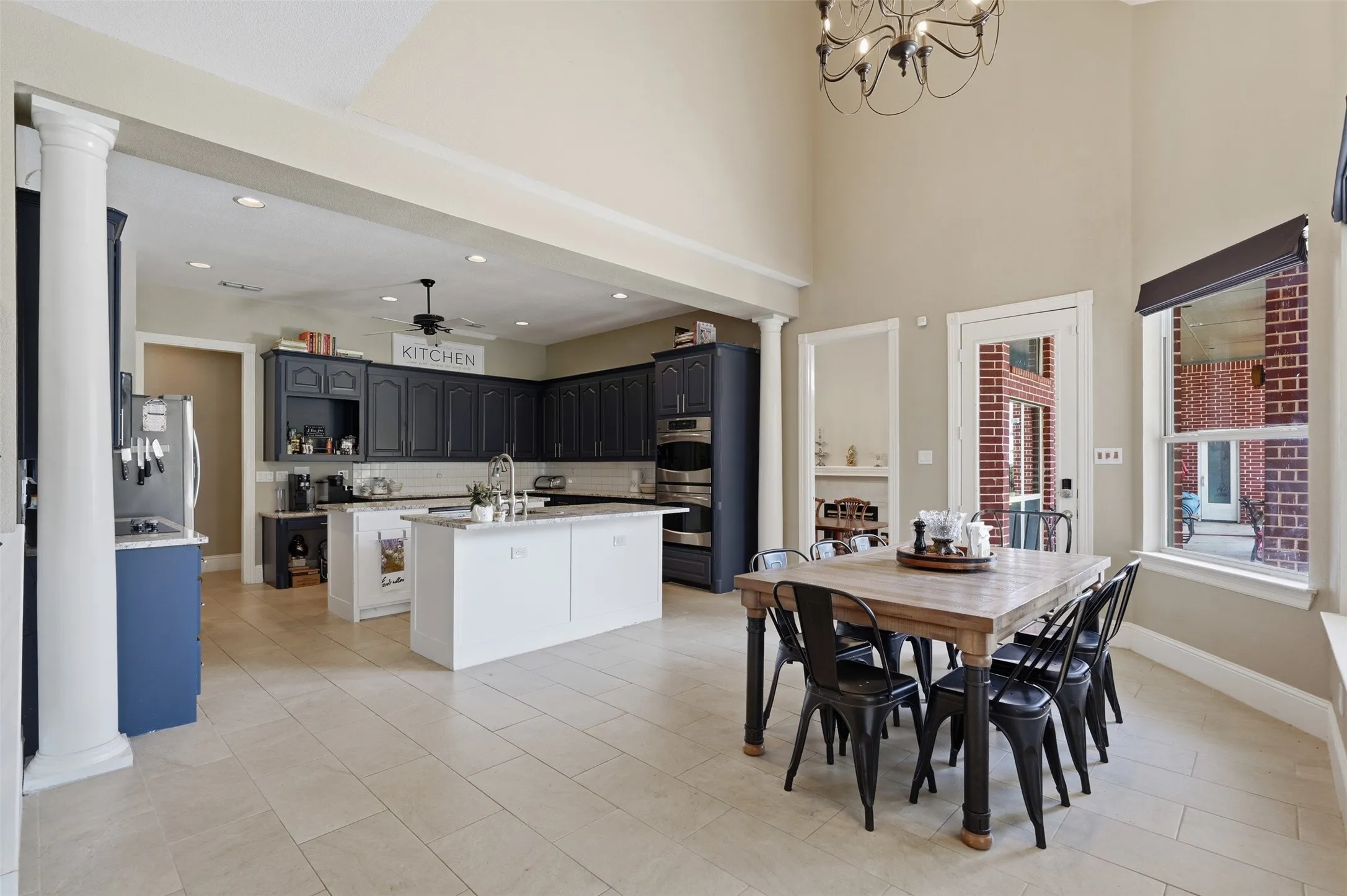 Spacious kitchen and dining area featuring high ceilings, light-toned tile flooring, and dark cabinetry