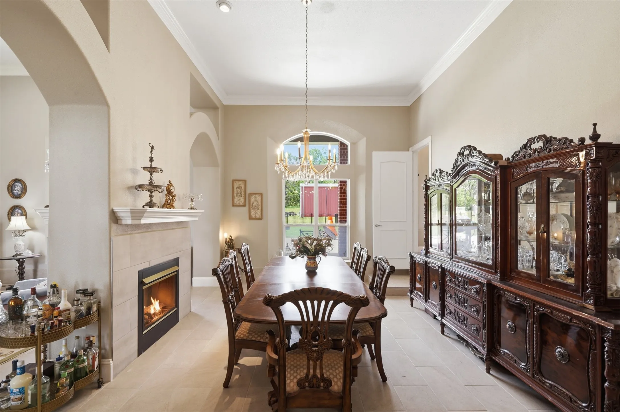 Spacious dining area featuring a fireplace with a light-toned tile surround and mantel, arched architectural details, recessed lighting, crown molding, and a chandelier