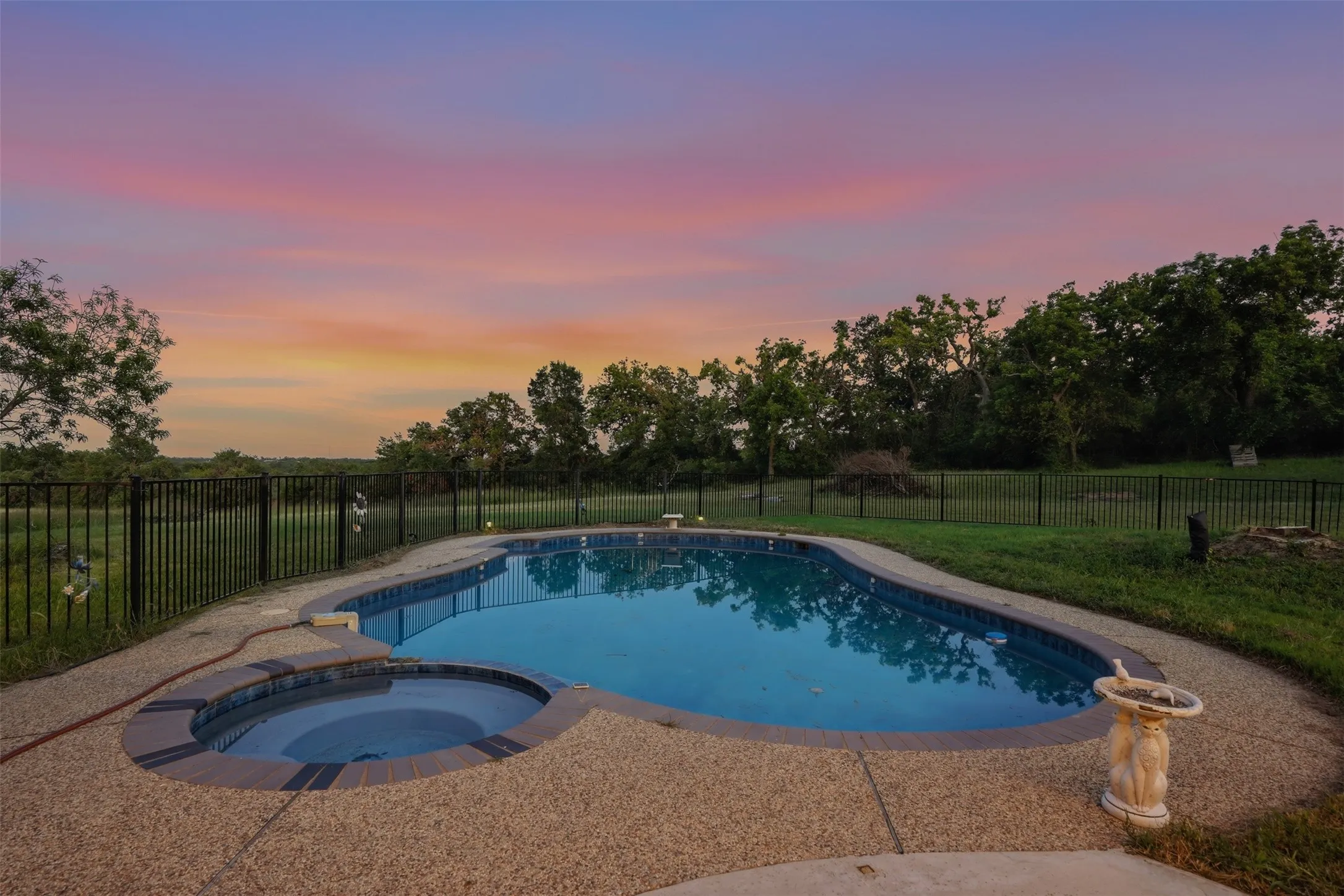 Kidney-shaped swimming pool featuring a built-in spa, aggregate concrete decking, and a black wrought-iron fence
