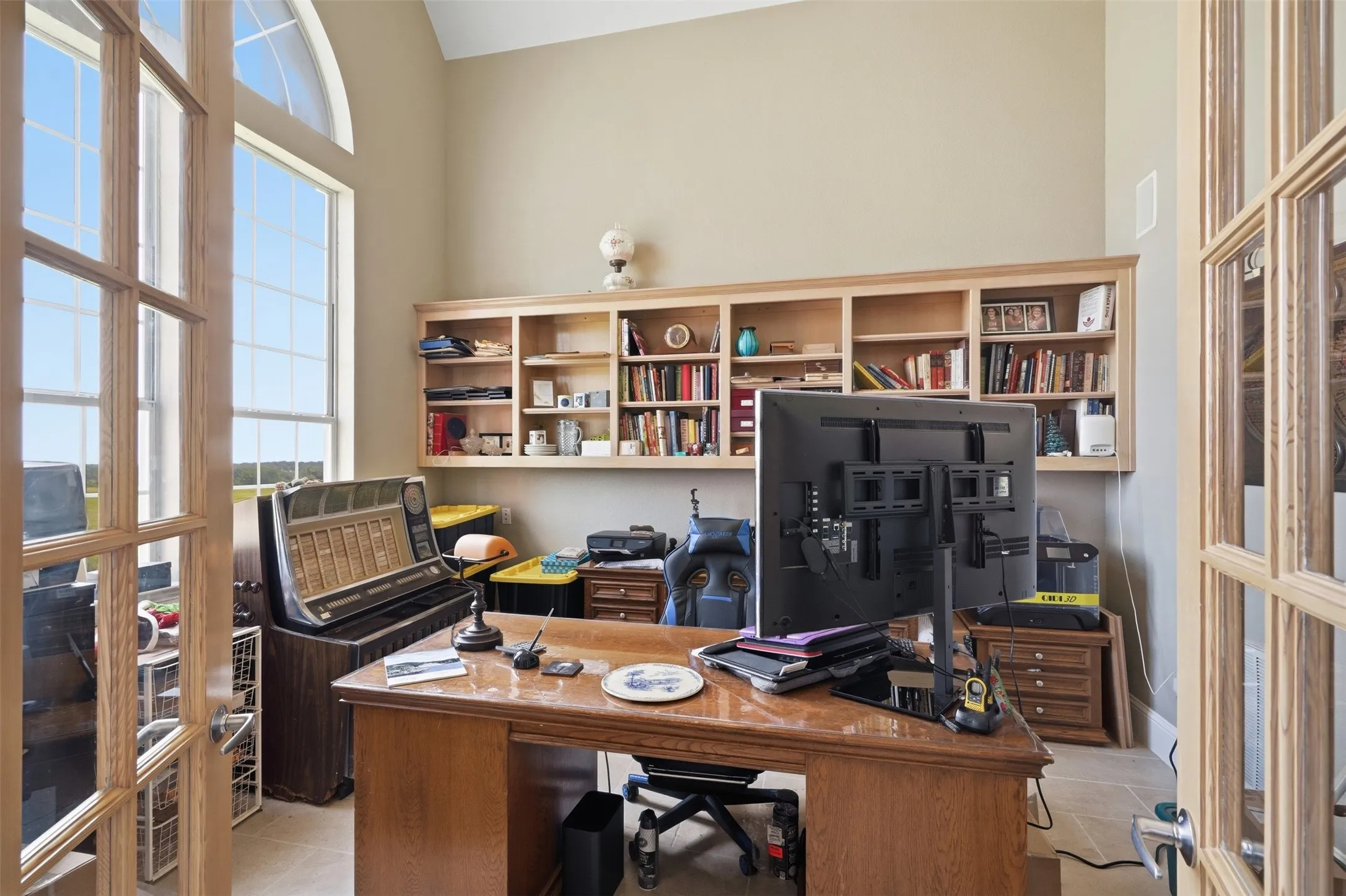 High ceilings and large windows define this room, featuring built-in shelving, French doors, and light-toned wall paint