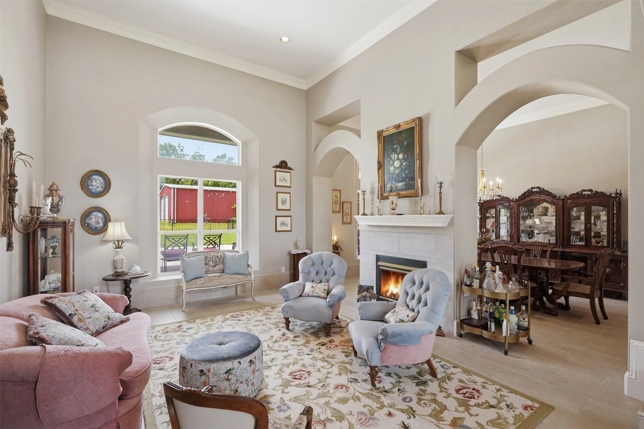 Spacious living area featuring a fireplace with a light-toned tile surround, arched architectural details, high vaulted ceilings, large windows, and tile flooring