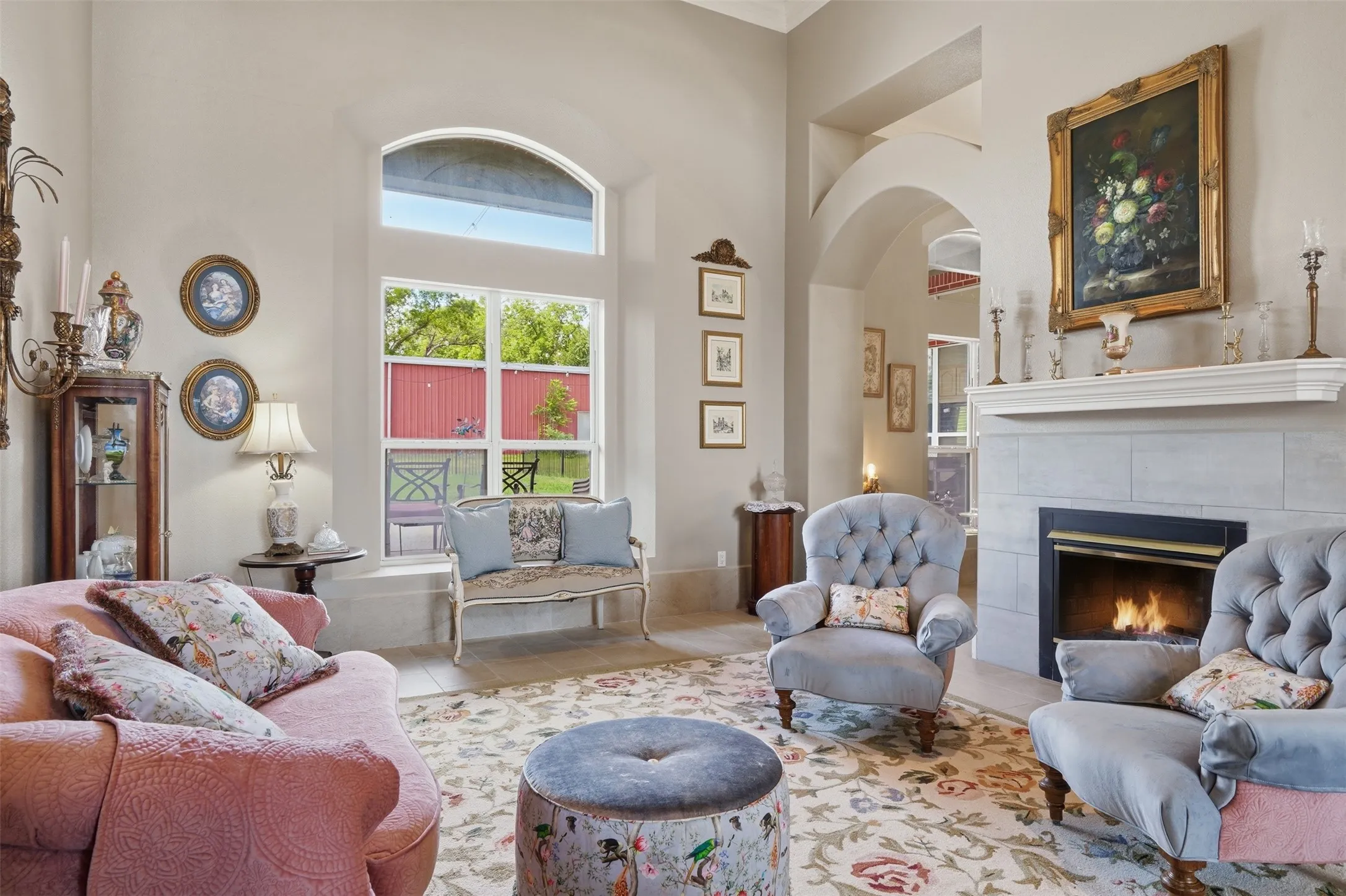 Spacious living area featuring a fireplace with a light-toned tile surround and mantle, arched doorways, a large window with an arched transom, and high ceilings