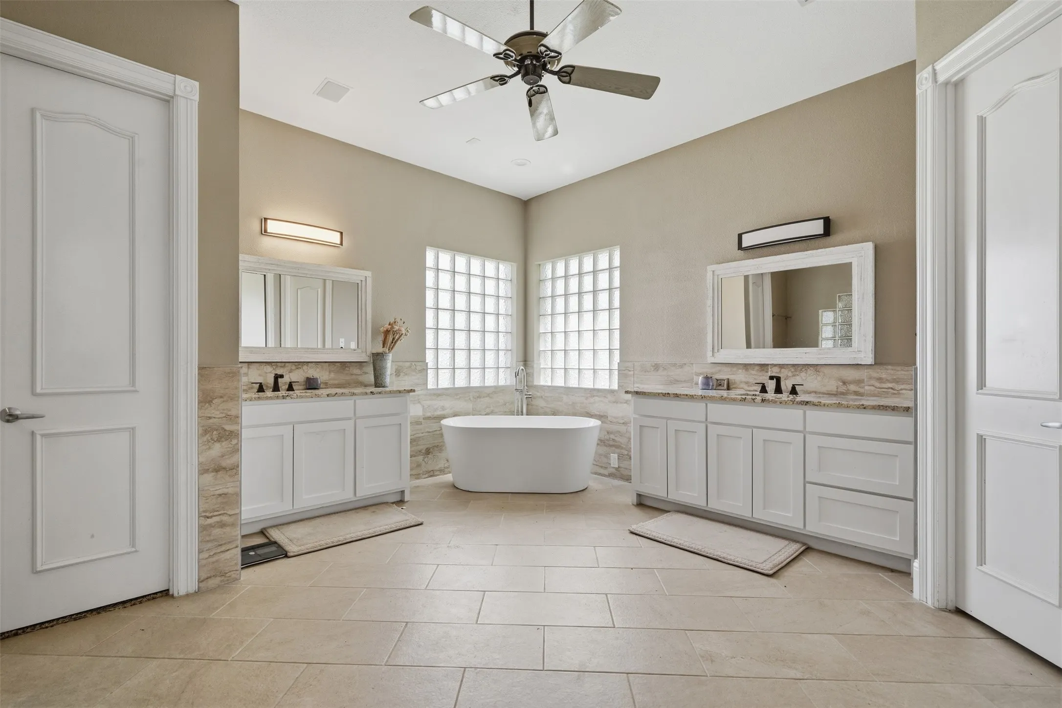 Spacious bathroom featuring a freestanding tub, dual vanity with shaker cabinets, tile flooring, and glass block windows