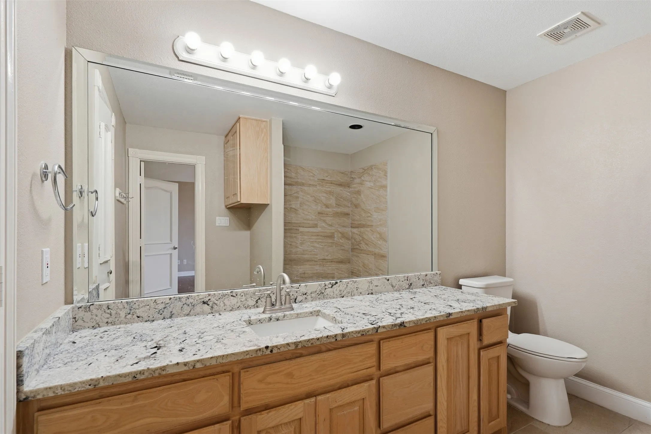 Bathroom vanity featuring a light-toned stone countertop, dual sinks, and light wood cabinetry