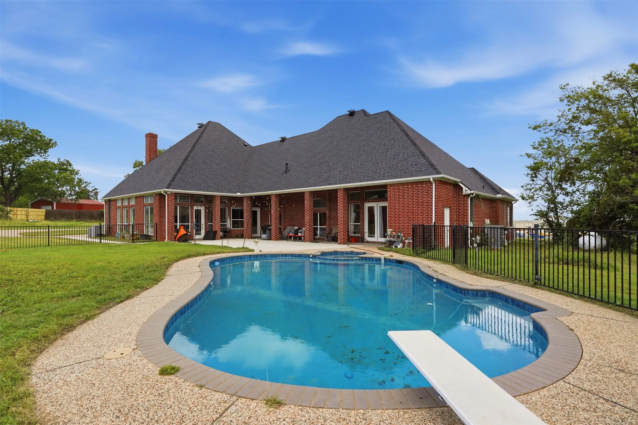 Expansive backyard featuring a large in-ground swimming pool with a diving board, brick exterior, covered patio, and perimeter fencing
