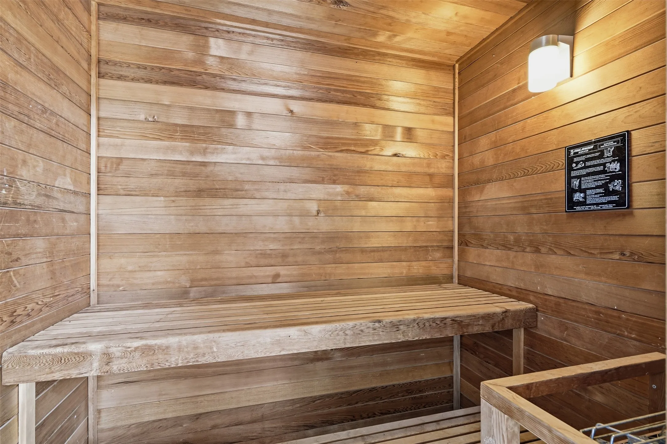 Sauna featuring natural wood paneling, built-in wooden benches, and a wall-mounted light fixture