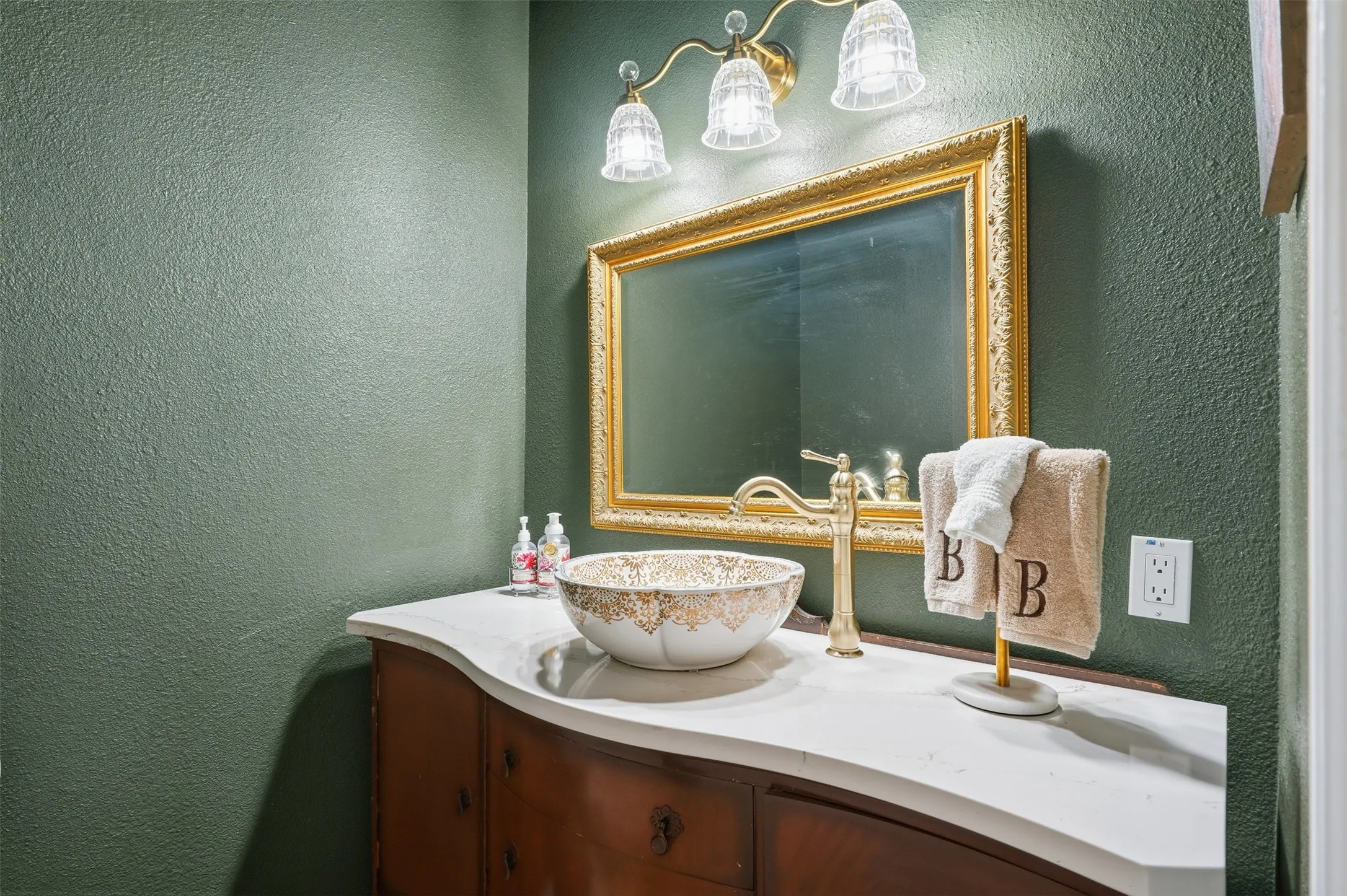 Custom vanity featuring a vessel sink, gold-tone faucet, and ornate gold-framed mirror