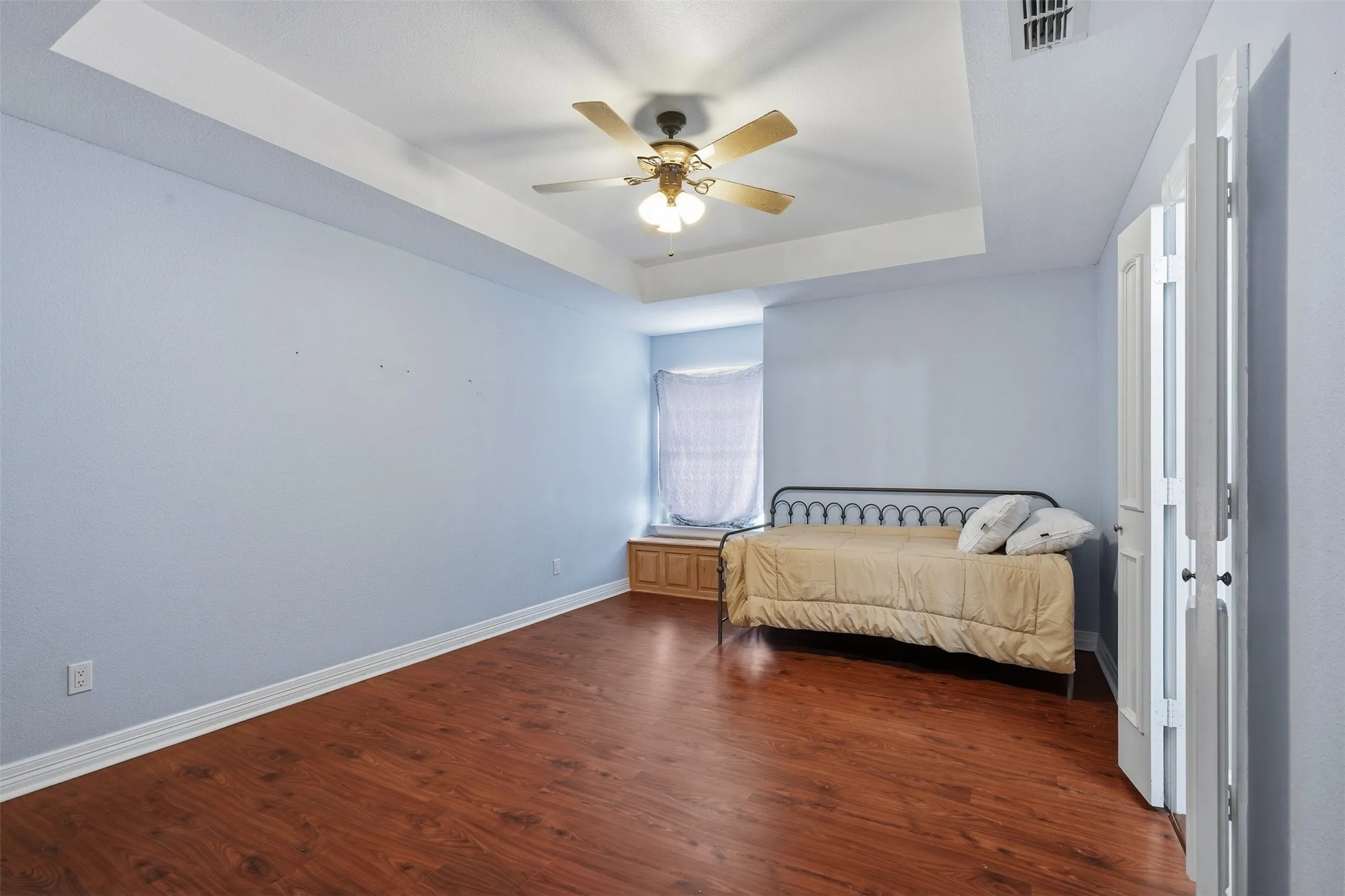 Spacious interior featuring wood-finish flooring, a tray ceiling, and a ceiling fan with integrated lighting