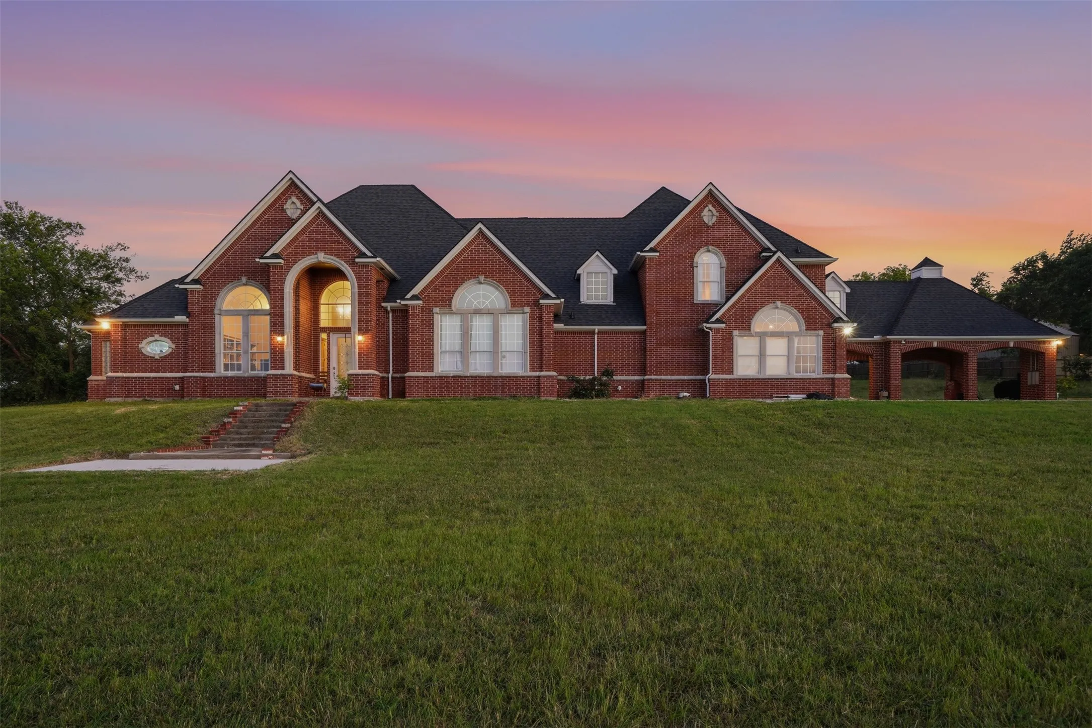 Brick exterior residence featuring a prominent arched entry, multiple gabled rooflines, and a covered porte-cochère