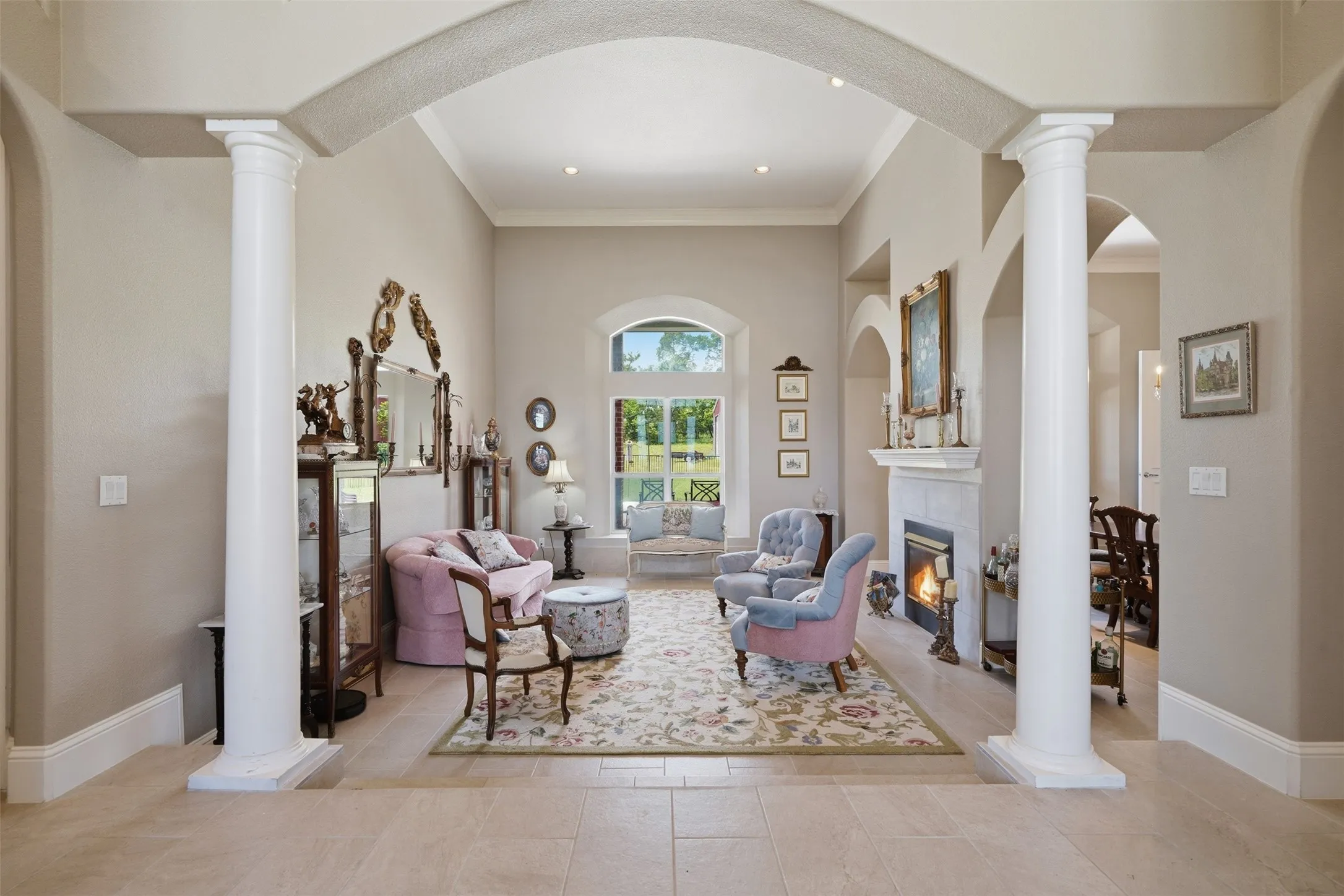 Spacious living area featuring architectural columns, elegant arched doorways, a built-in fireplace with a mantel, high vaulted ceilings, and large arched windows providing abundant natural light