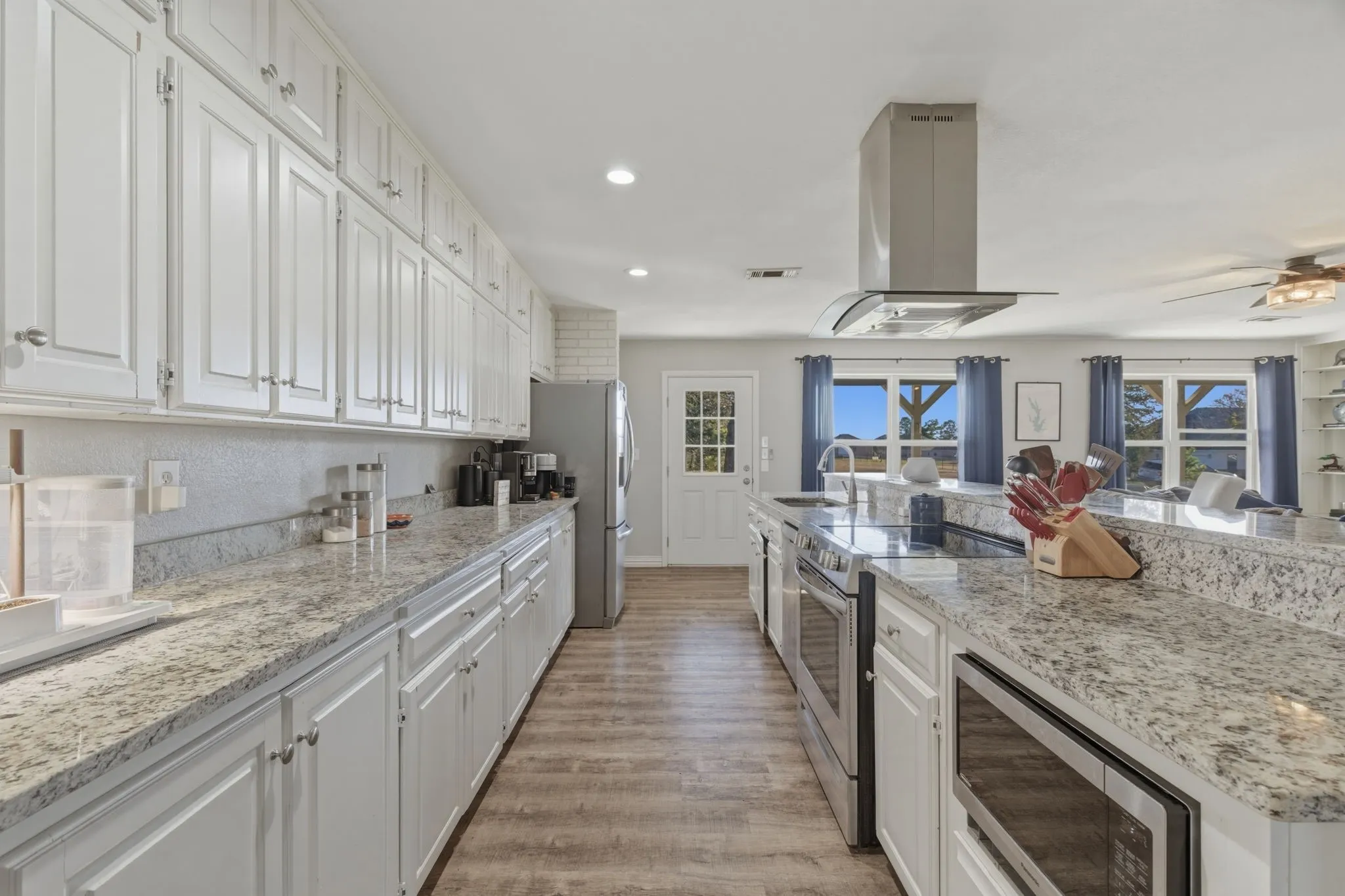Kitchen with white cabinets, stainless steel appliances, island exhaust hood, recessed lighting, and light stone countertops