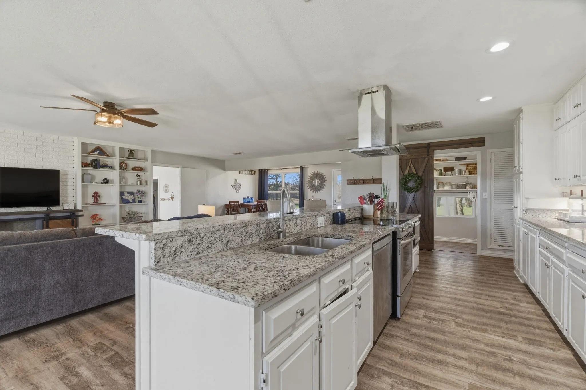 Kitchen with open floor plan, white cabinets, light stone countertops, island exhaust hood, and light wood-style flooring