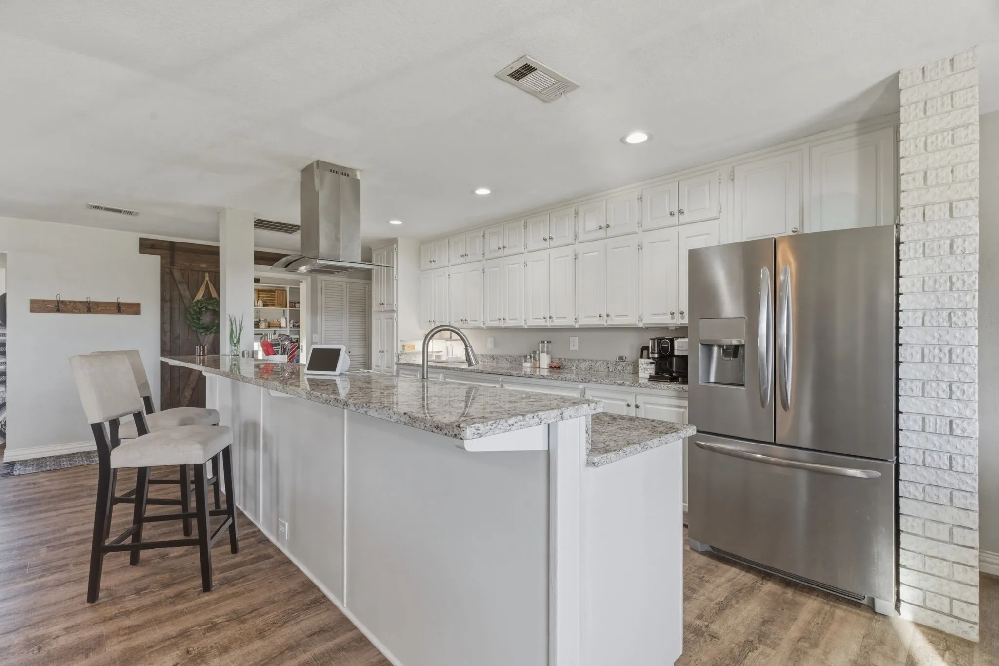 Kitchen with stainless steel refrigerator with ice dispenser, white cabinetry, dark wood-style flooring, a large island with sink, and light stone countertops
