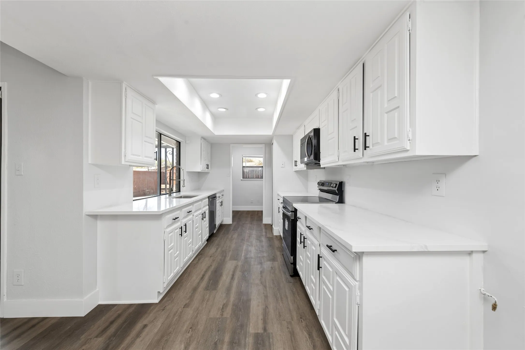 Kitchen featuring stainless steel appliances, recessed lighting, white cabinetry, dark wood-type flooring, and a raised ceiling