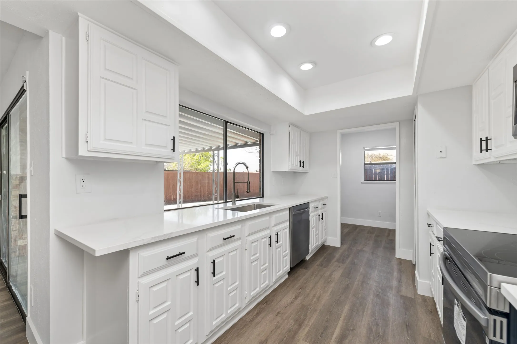 Kitchen with white cabinetry, stainless steel appliances, recessed lighting, dark wood-style flooring, and light stone countertops