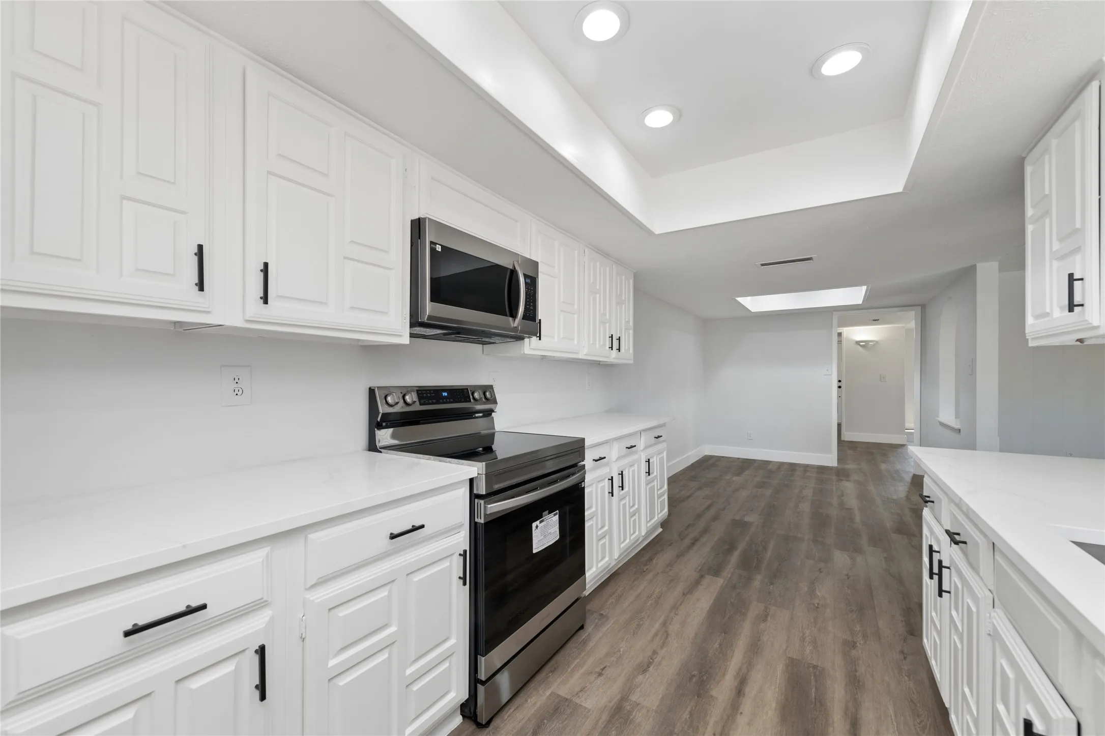 Kitchen featuring stainless steel appliances, white cabinets, dark wood-style floors, recessed lighting, and a tray ceiling