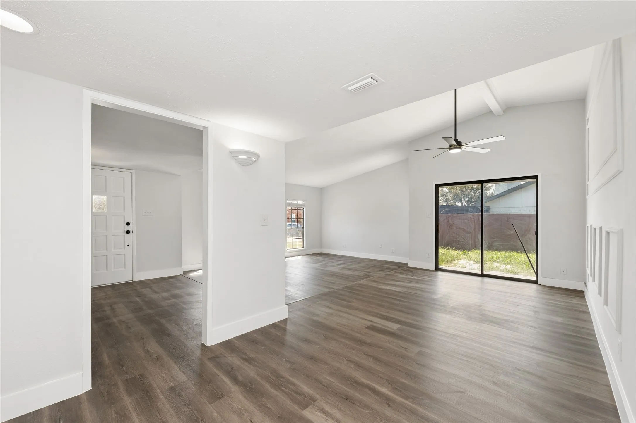 Unfurnished room featuring dark wood-type flooring, healthy amount of natural light, lofted ceiling, and a ceiling fan