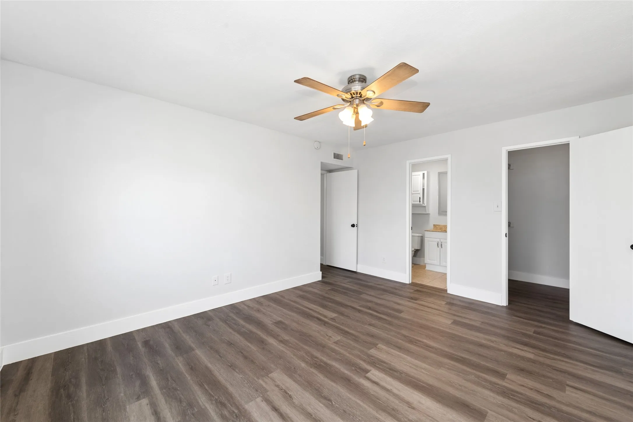 Unfurnished bedroom featuring a ceiling fan, dark wood-type flooring, a spacious closet, and ensuite bath