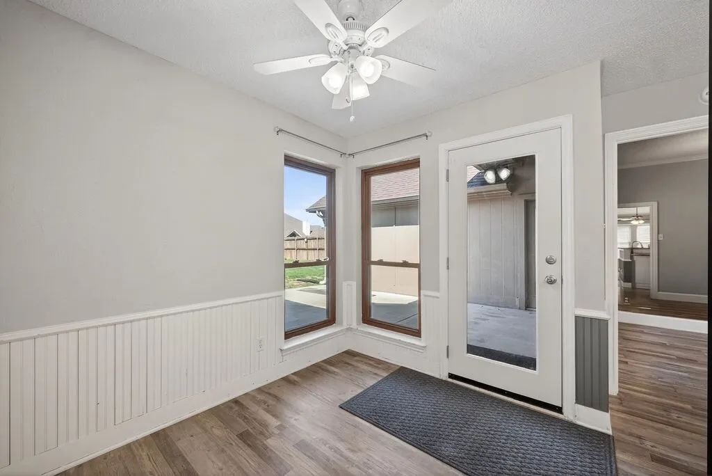 Entryway featuring a ceiling fan, a textured ceiling, wood finished floors, and wainscoting