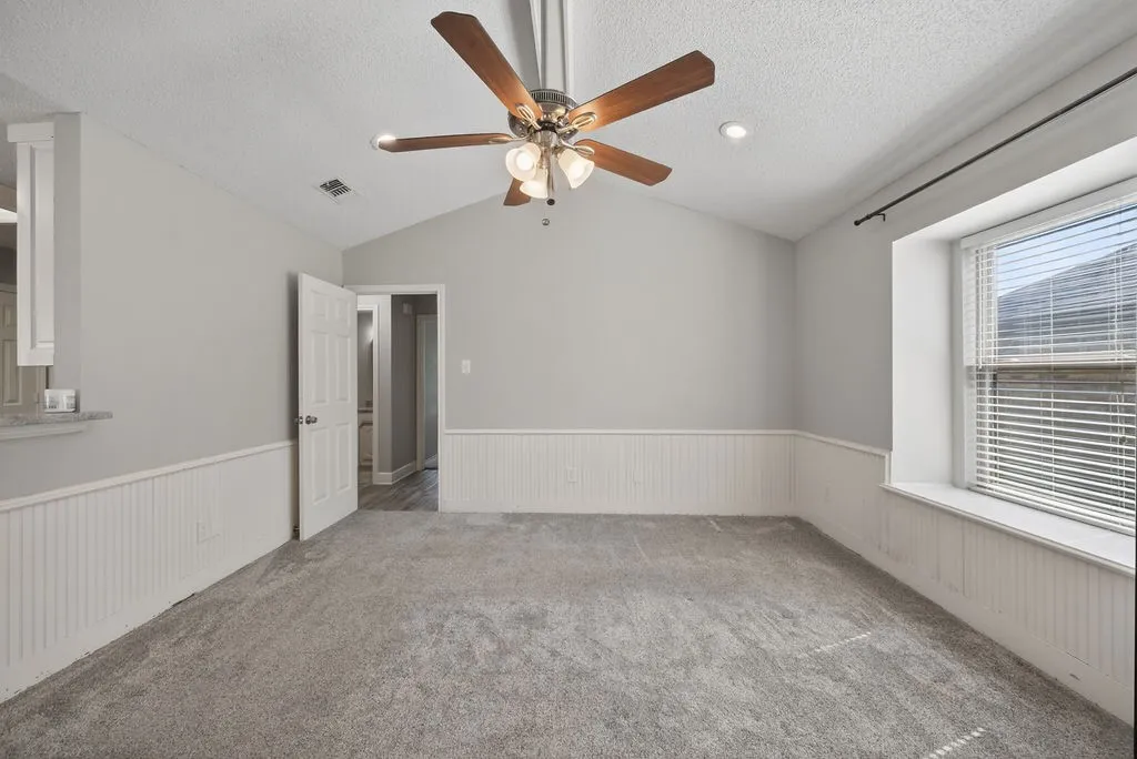Carpeted spare room featuring a ceiling fan, a textured ceiling, and a wainscoted wall