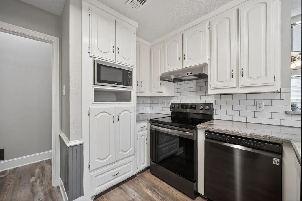 Kitchen with stainless steel appliances, white cabinets, light stone countertops, a textured ceiling, and tasteful backsplash