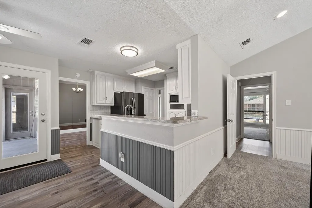 Kitchen with white cabinets, a peninsula, a ceiling fan, black refrigerator with ice dispenser, and wainscoting