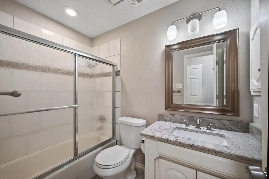 Bathroom featuring a textured wall, vanity, enclosed tub / shower combo, a textured ceiling, and recessed lighting