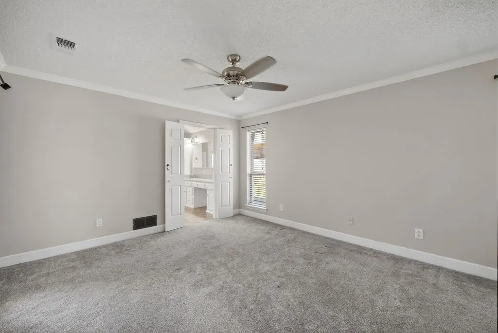 Unfurnished bedroom featuring a textured ceiling, crown molding, light carpet, ceiling fan, and ensuite bathroom
