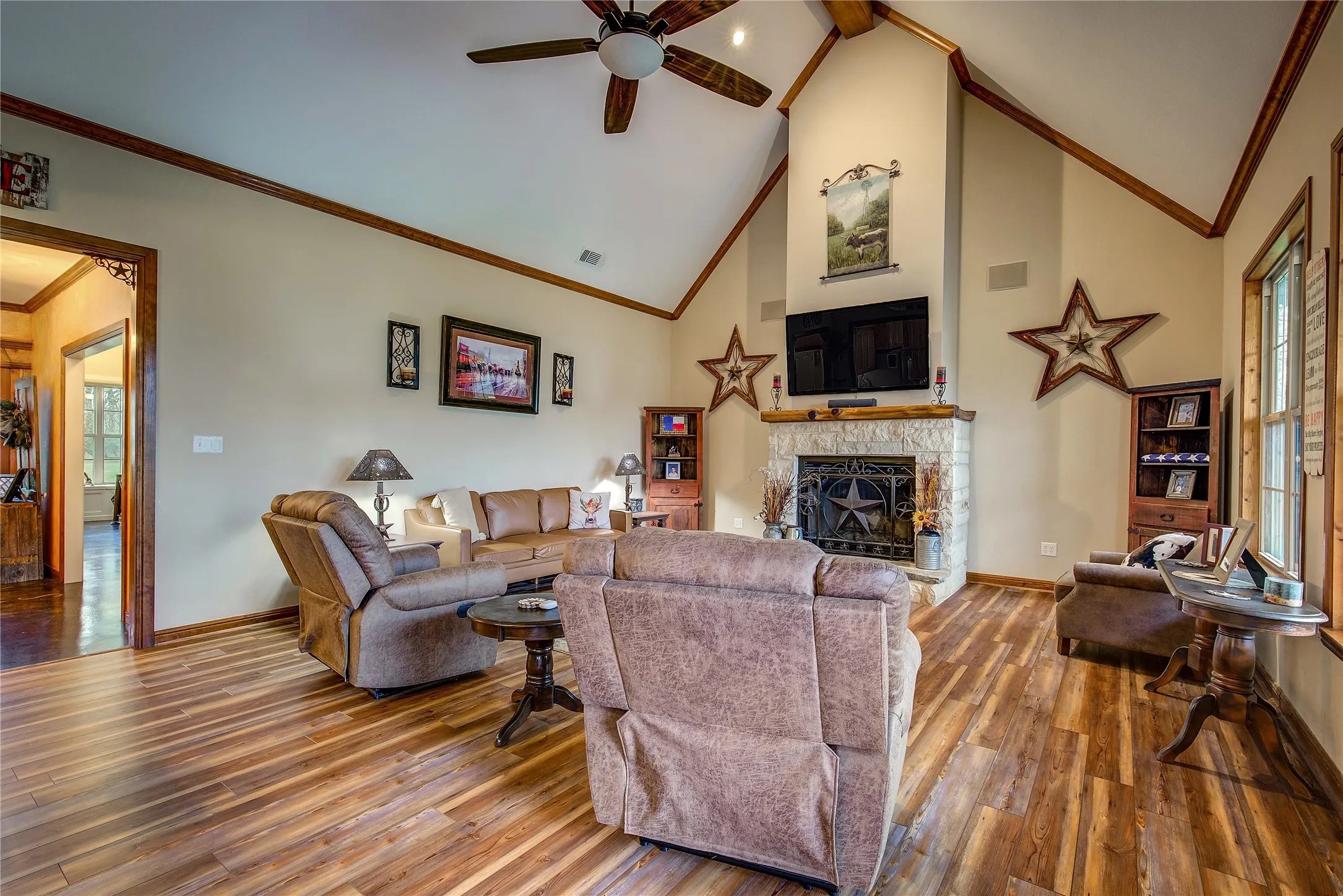Living room featuring soaring ceilings, a stone wood-burning fireplace, newly finished wood flooring, and large windows that fill the space with natural light and beautiful countryside views.