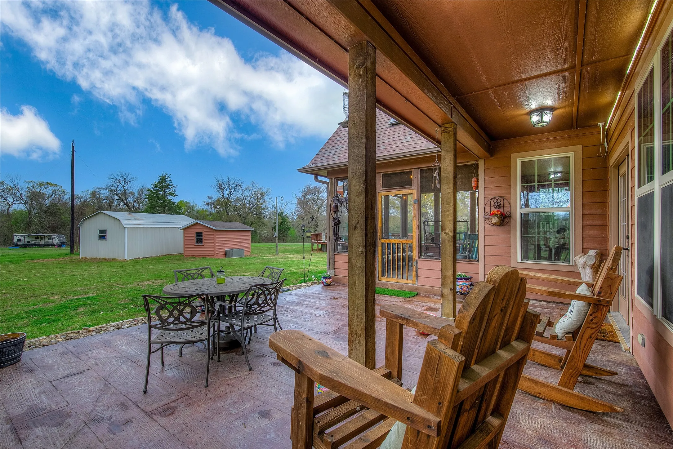 View of the back patio featuring an outdoor dining area and storage outbuildings.
