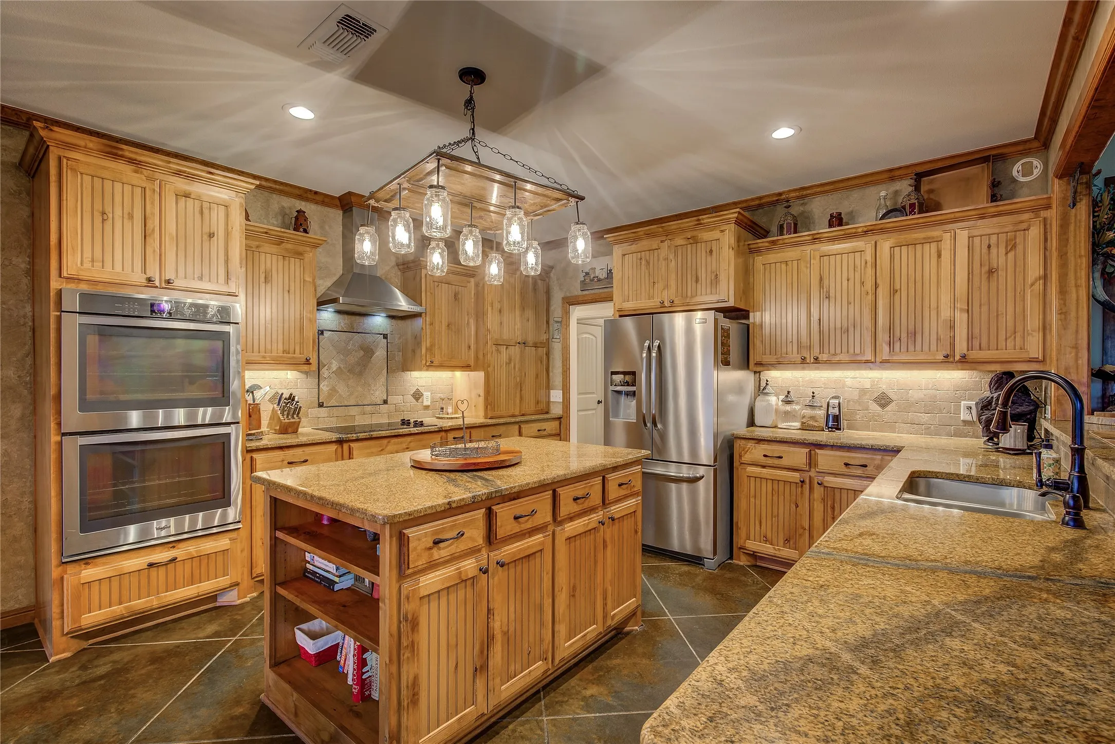 Gourmet eat-in kitchen measuring 23’5” x 14’3”, featuring a large island, double ovens, cooktop, appliance garage, breakfast bar, and custom upgrades throughout.