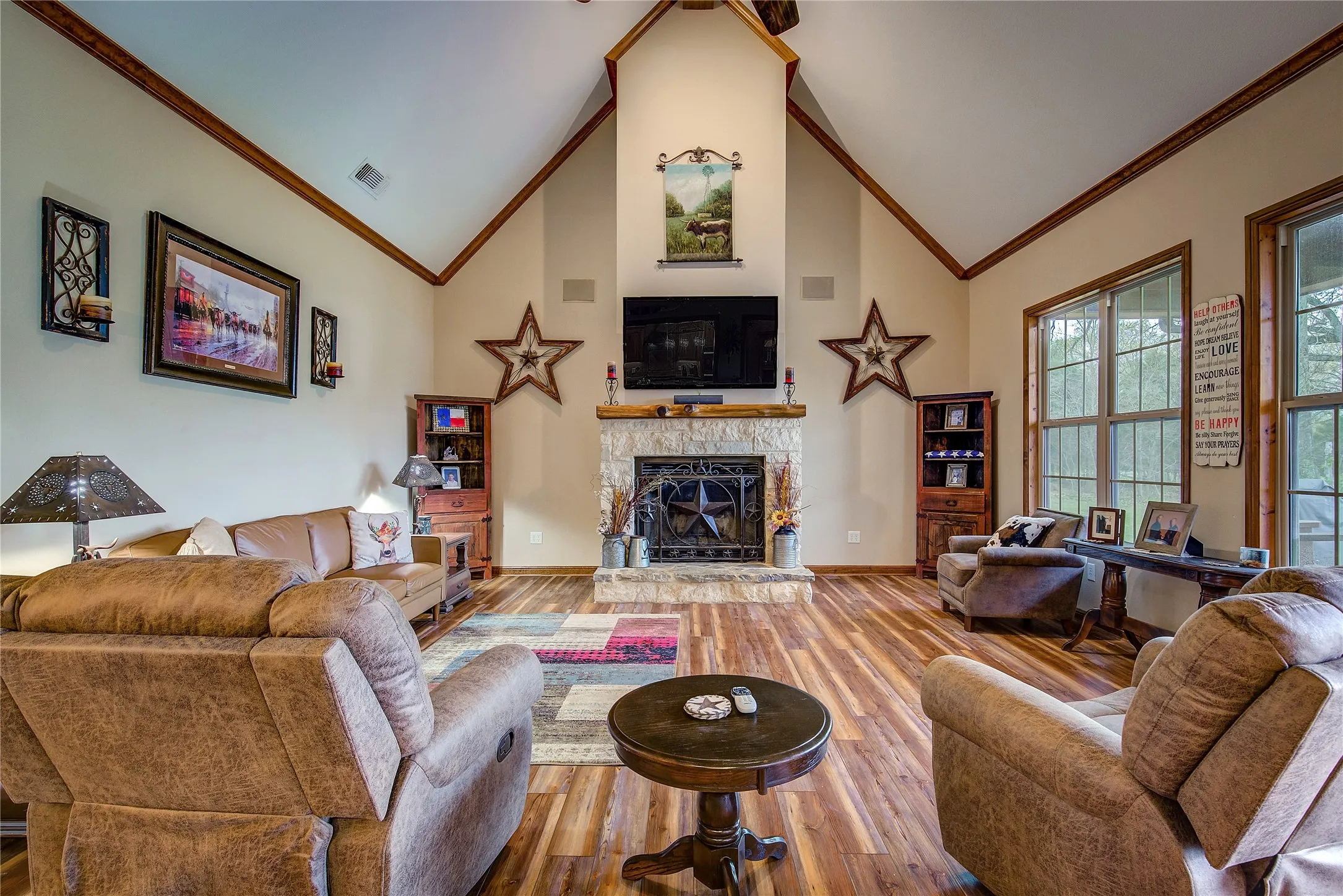 Living room featuring soaring ceilings, a stone wood-burning fireplace, newly finished wood flooring, and large windows that fill the space with natural light and beautiful countryside views.