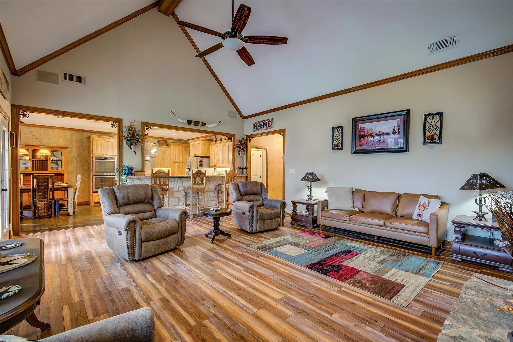 Living room featuring soaring ceilings, a stone wood-burning fireplace, newly finished wood flooring, and large windows that fill the space with natural light and beautiful countryside views.