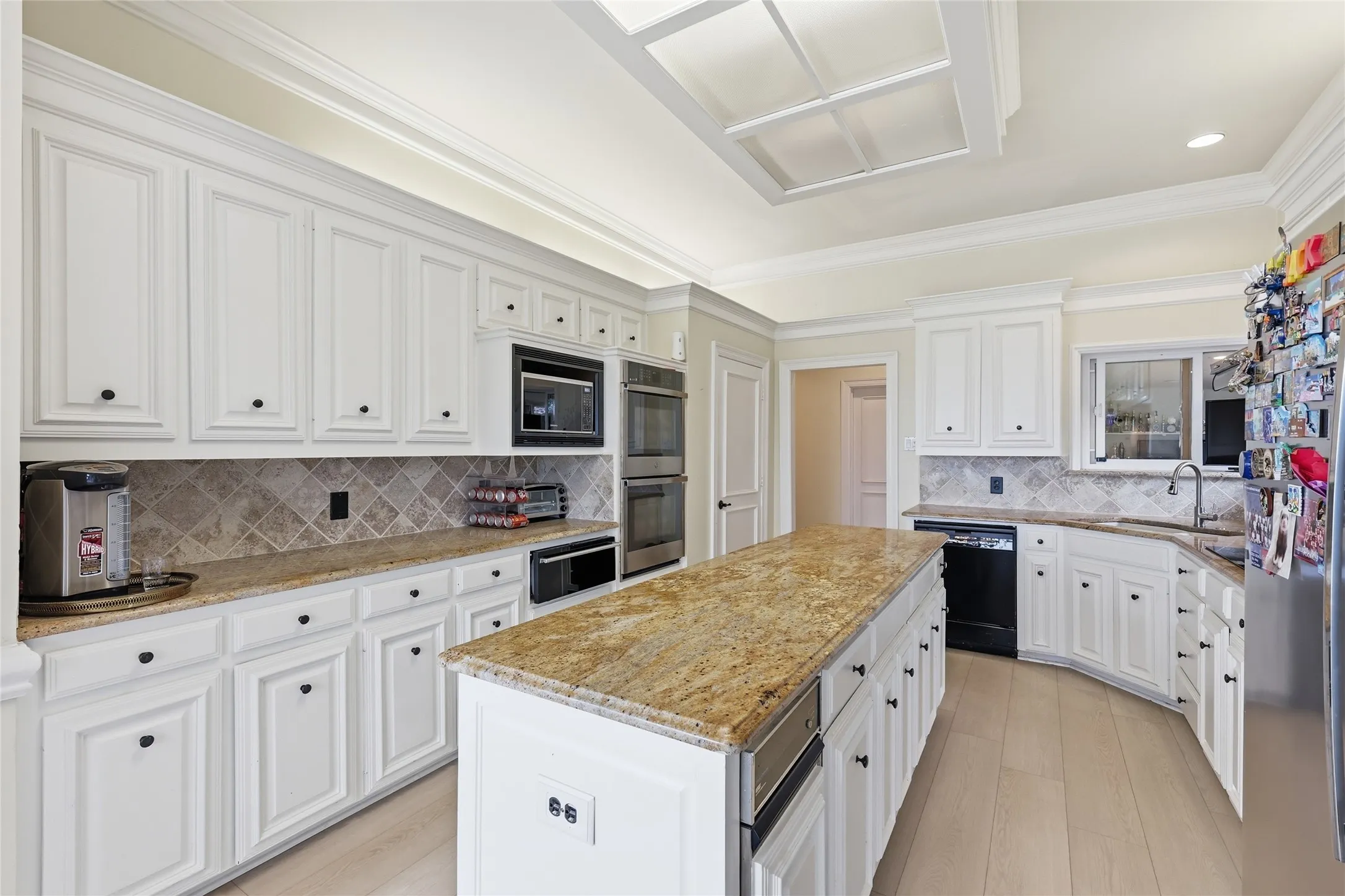 Kitchen with crown molding, light stone countertops, white cabinets, a center island, and black appliances