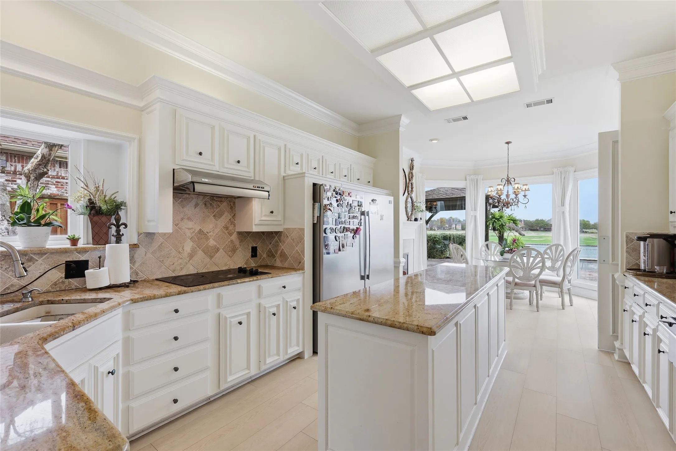 Kitchen with light stone countertops, healthy amount of natural light, ornamental molding, a center island, and white cabinets