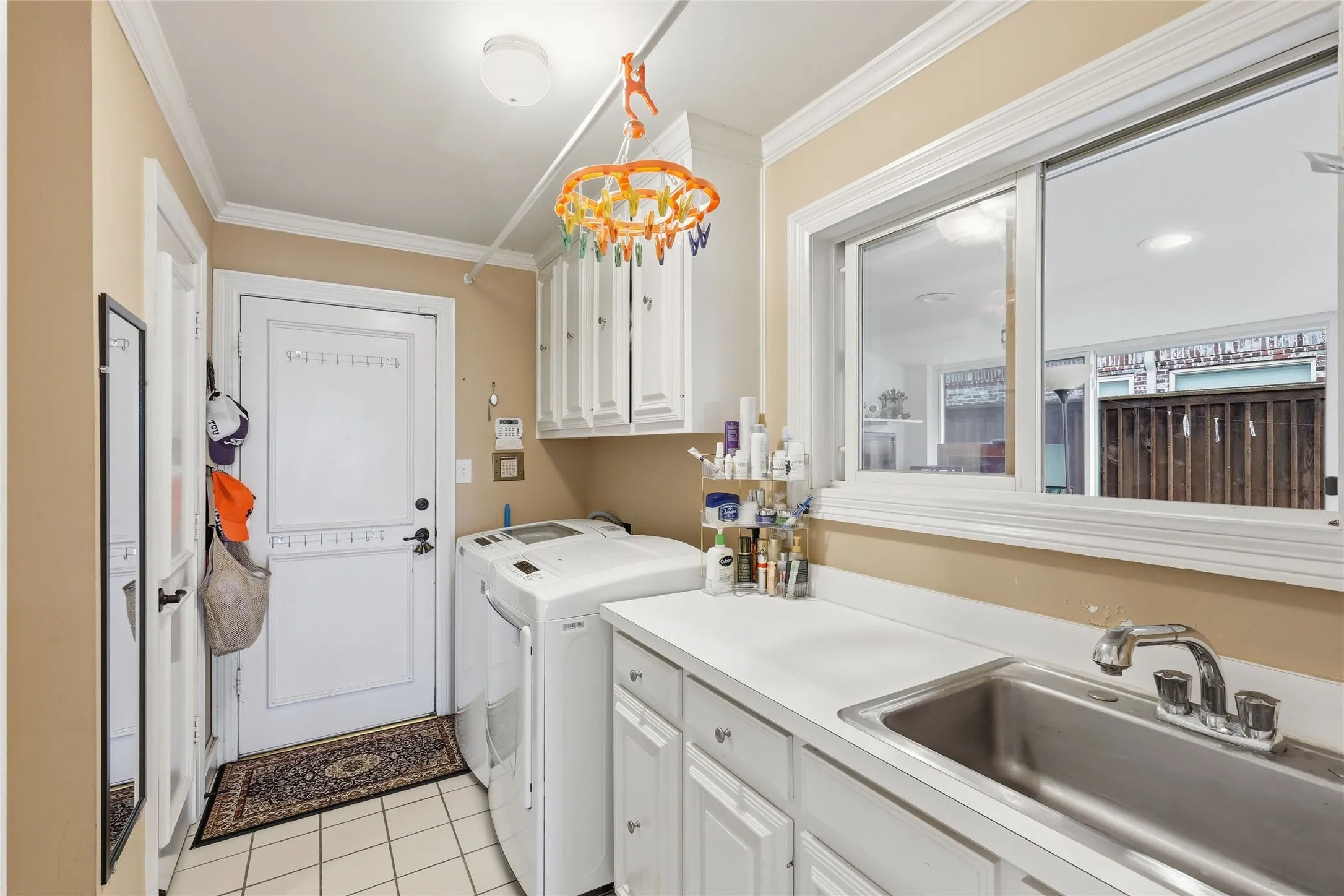 Laundry area with cabinet space, light tile patterned floors, washer and clothes dryer, and ornamental molding