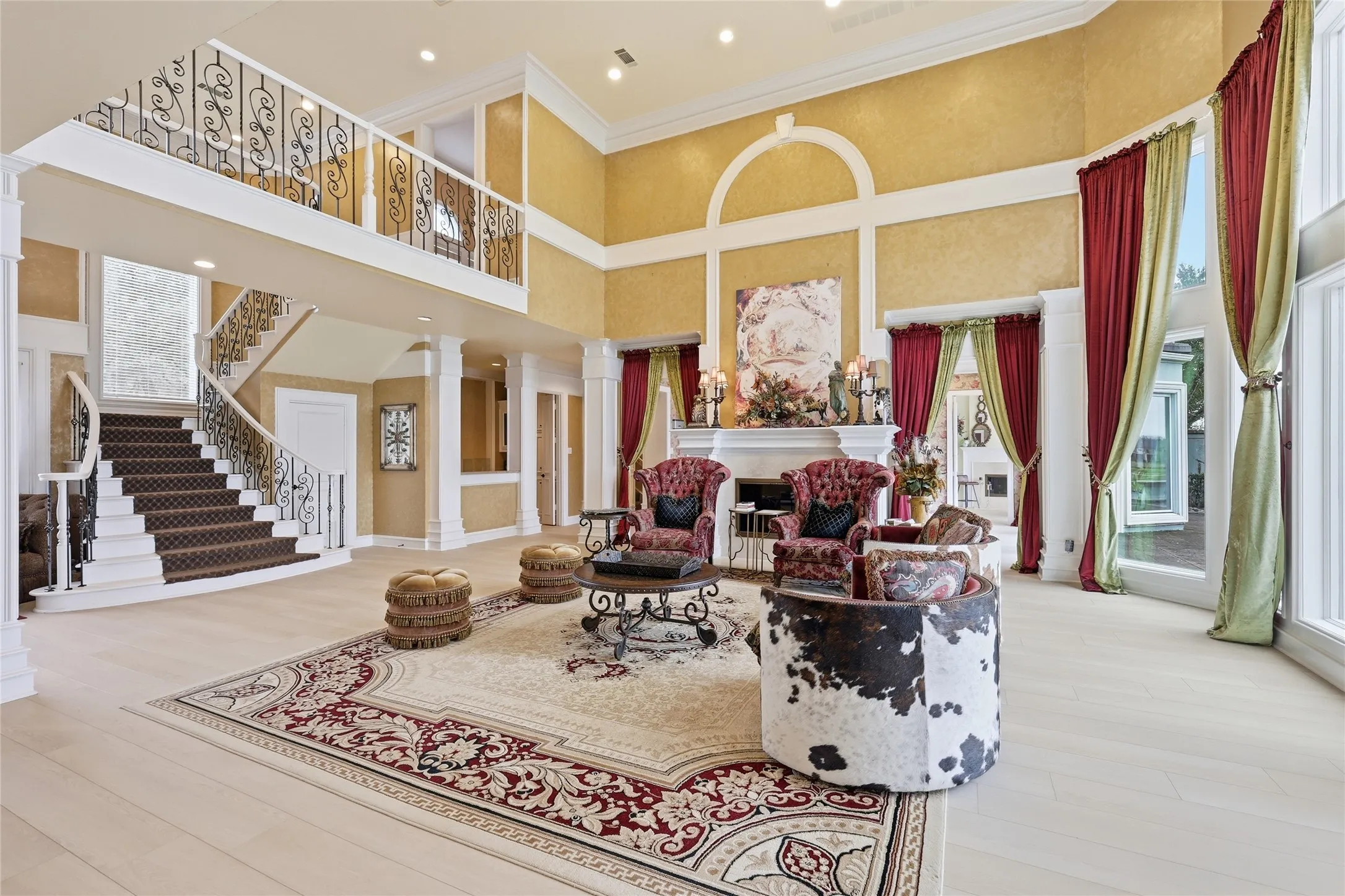Living area with ornate columns, ornamental molding, a high ceiling, light wood-style flooring, and a fireplace