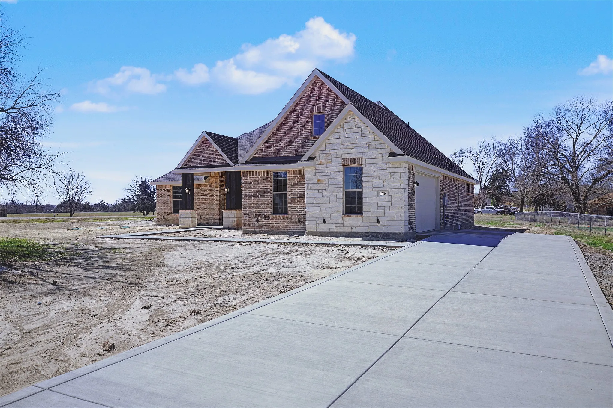 View of front facade with brick siding, stone siding, a garage, and driveway