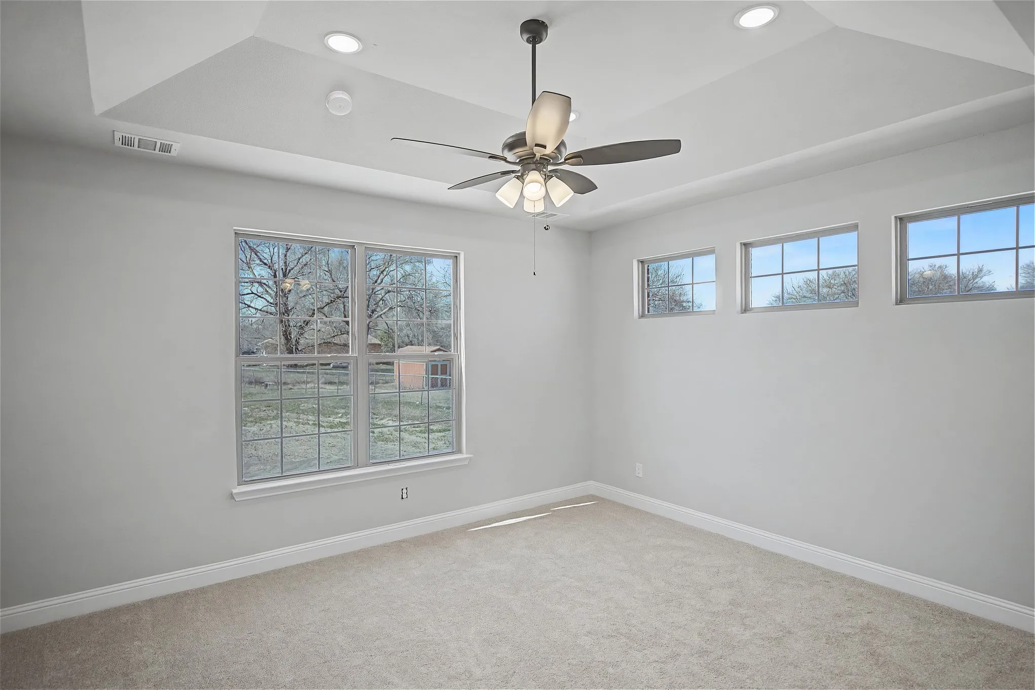 Carpeted empty room featuring ceiling fan, a raised ceiling, and recessed lighting