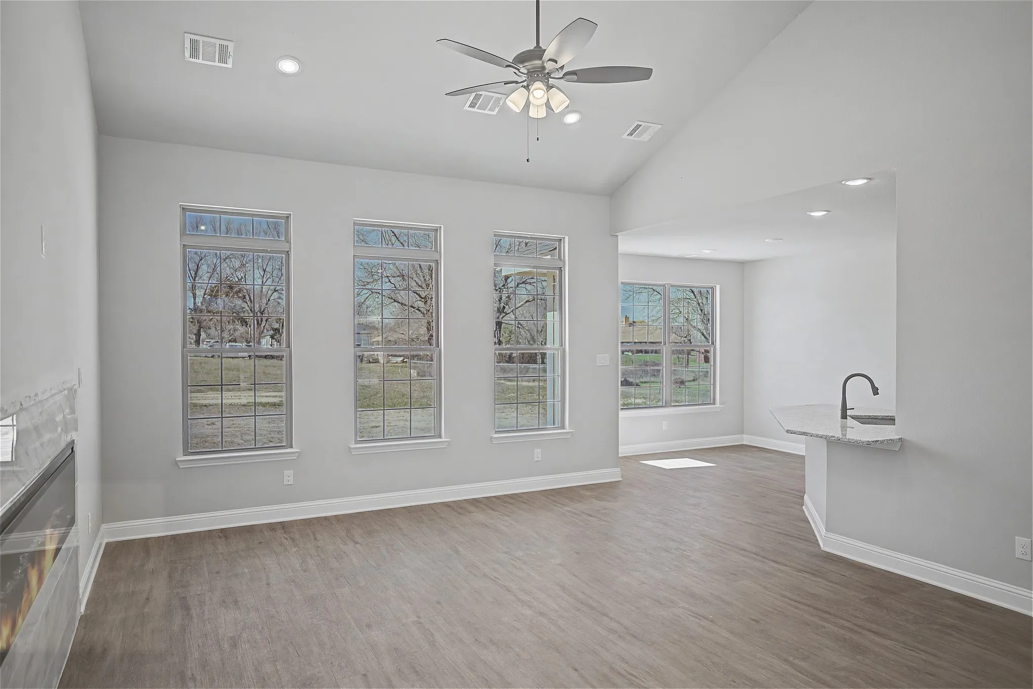 Unfurnished living room featuring light wood-style floors, a ceiling fan, vaulted ceiling, a glass covered fireplace, and recessed lighting