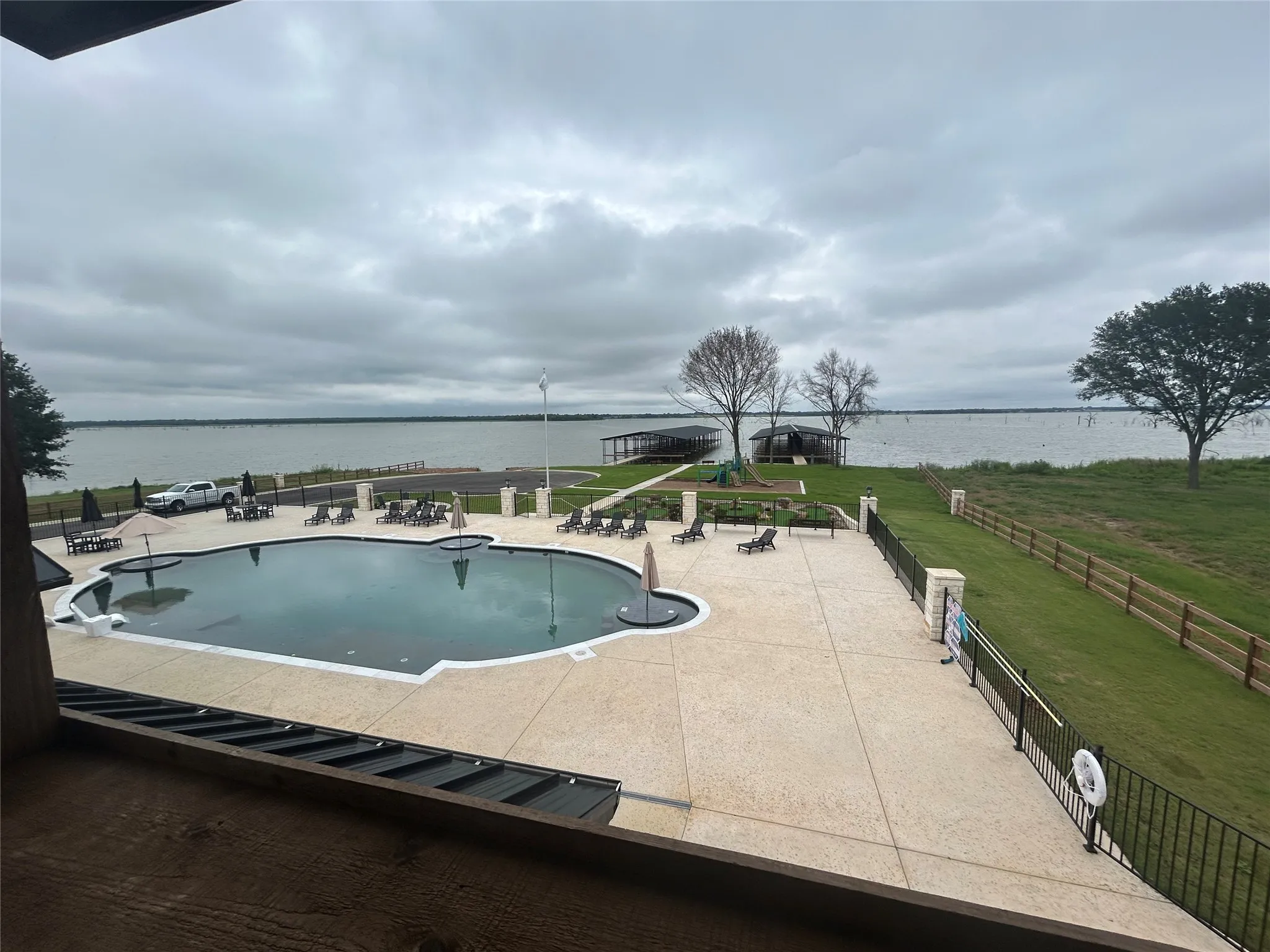 Resort-style pool area featuring a freeform swimming pool with integrated spa, expansive concrete decking, and surrounding black metal fencing