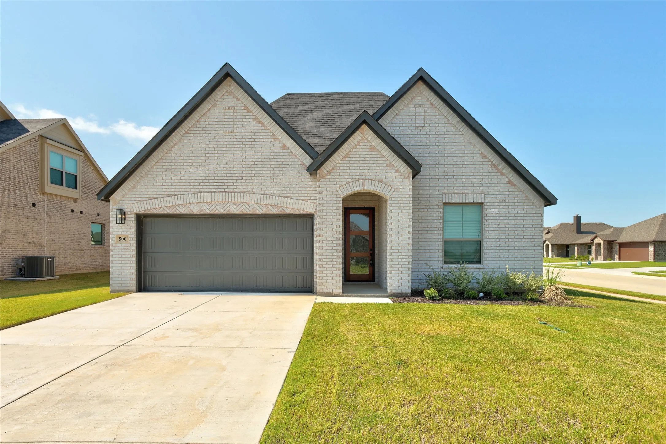 Light-colored brick exterior featuring dark trim, an arched entry, and a prominent dark garage door