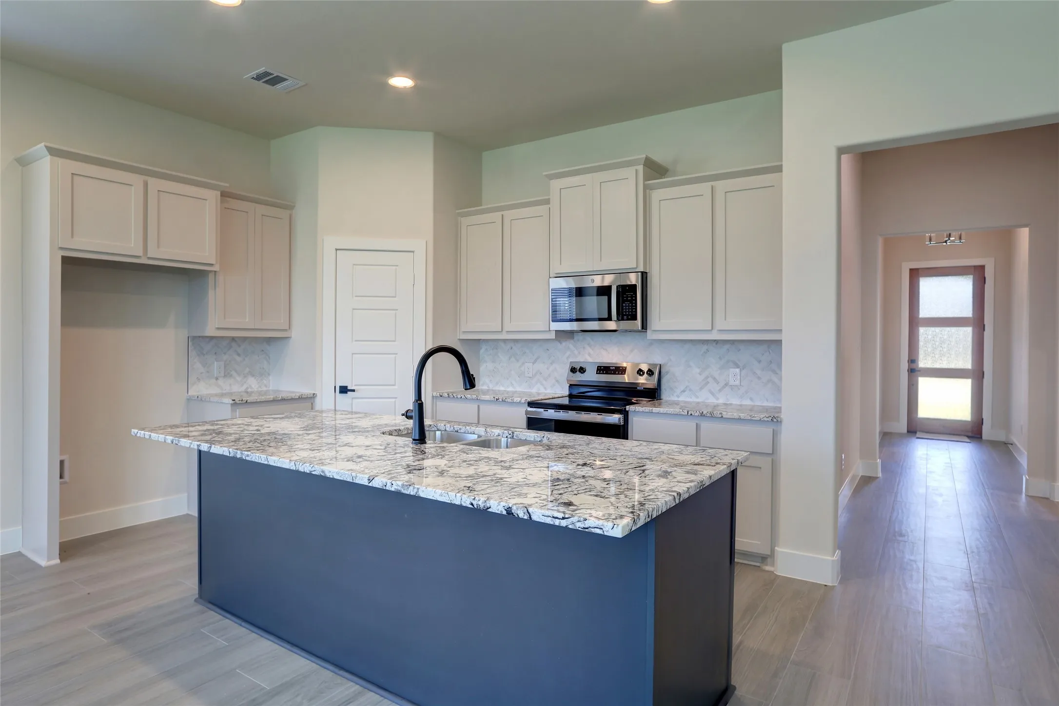 Kitchen featuring a central island with granite countertop, light-toned cabinetry, stainless steel appliances, and a chevron pattern tile backsplash