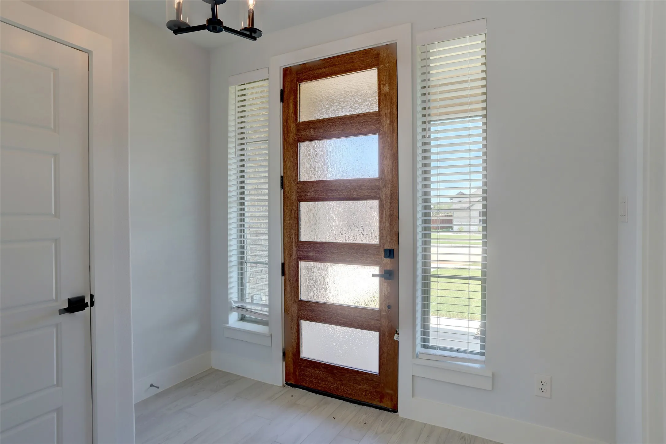 Entryway featuring a five-panel wood-finish door with textured privacy glass, flanked by vertical windows with blinds