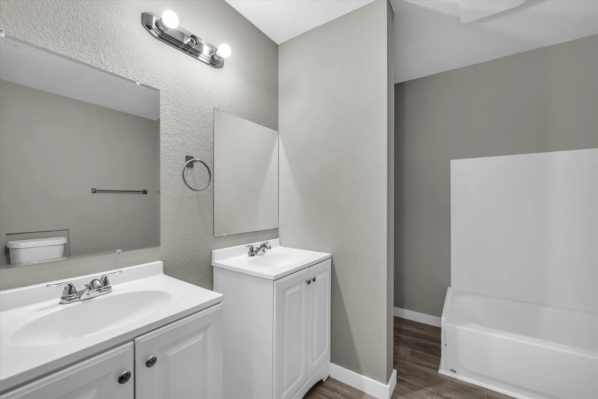 Primary bathroom with two vanities, a textured wall and a bathtub