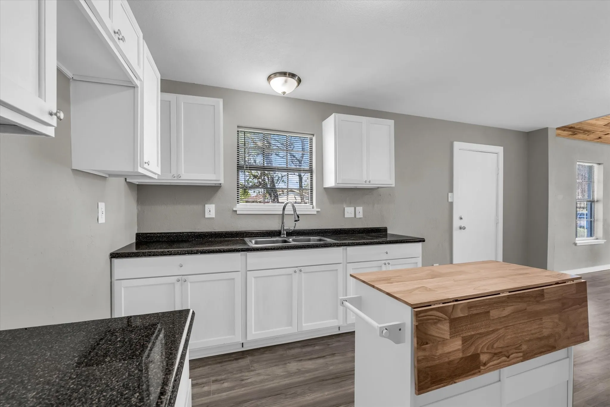 Kitchen with dark wood-style floors, white cabinets, dark countertops and a kitchen island