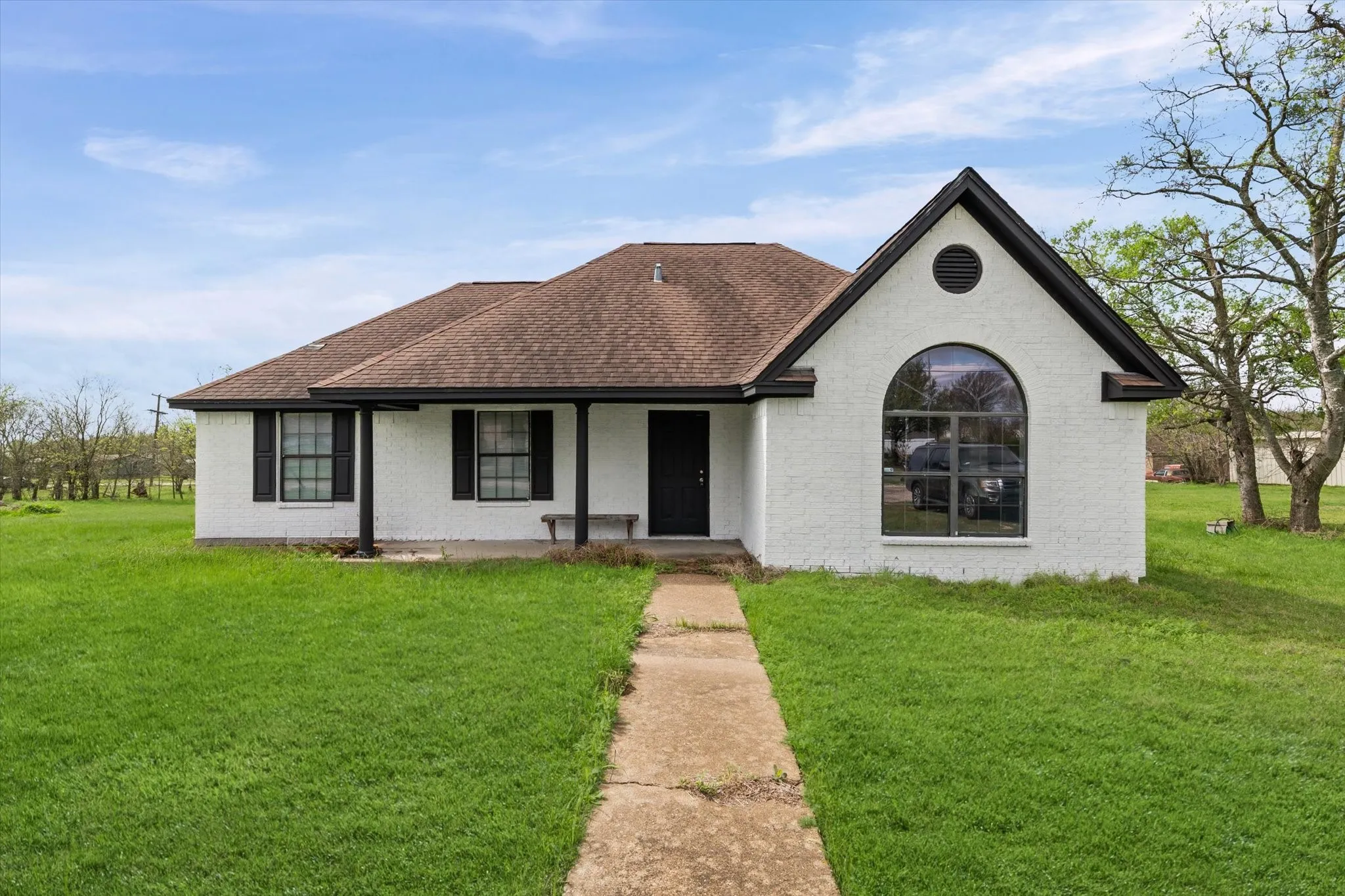 View of front of home with a front yard, brick siding, roof with shingles, and covered porch