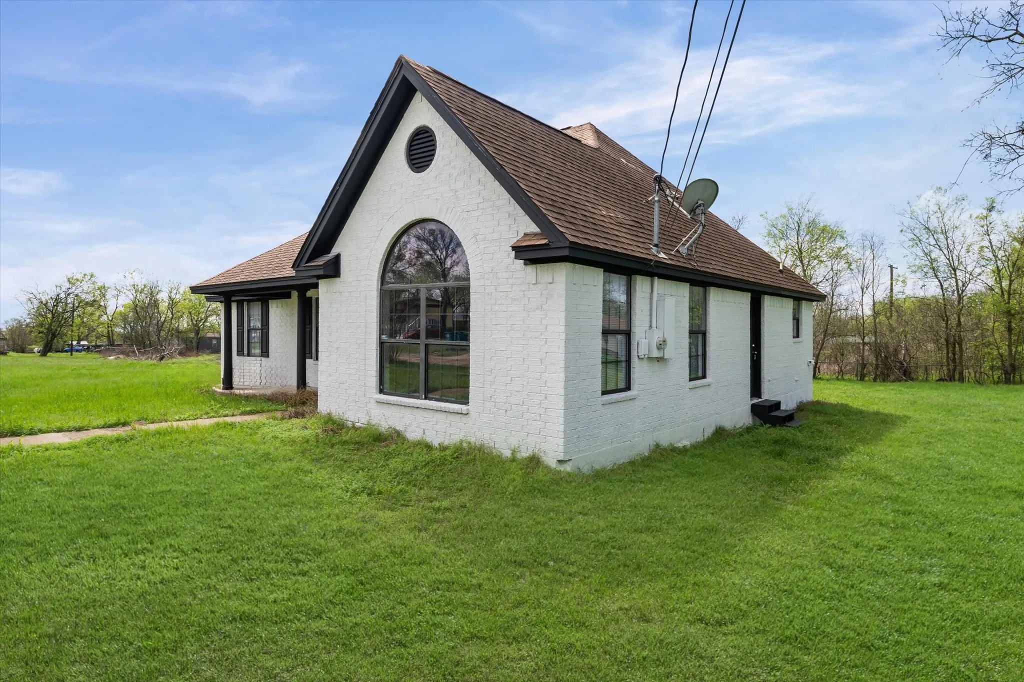 View of property exterior featuring brick siding, a lawn, and roof with shingles