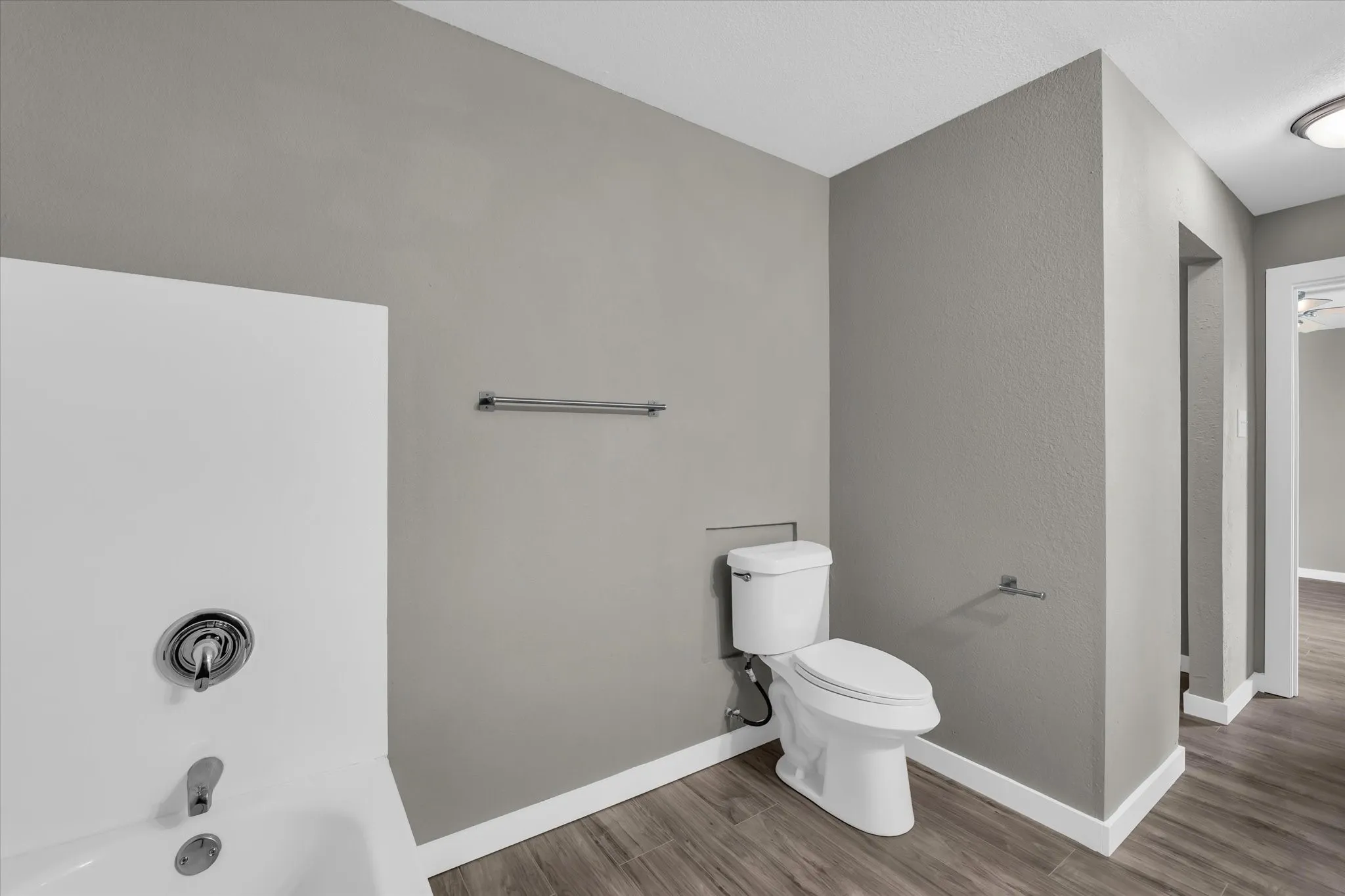 Primary bathroom featuring a tub to relax in, dark wood-style flooring, and a textured wall