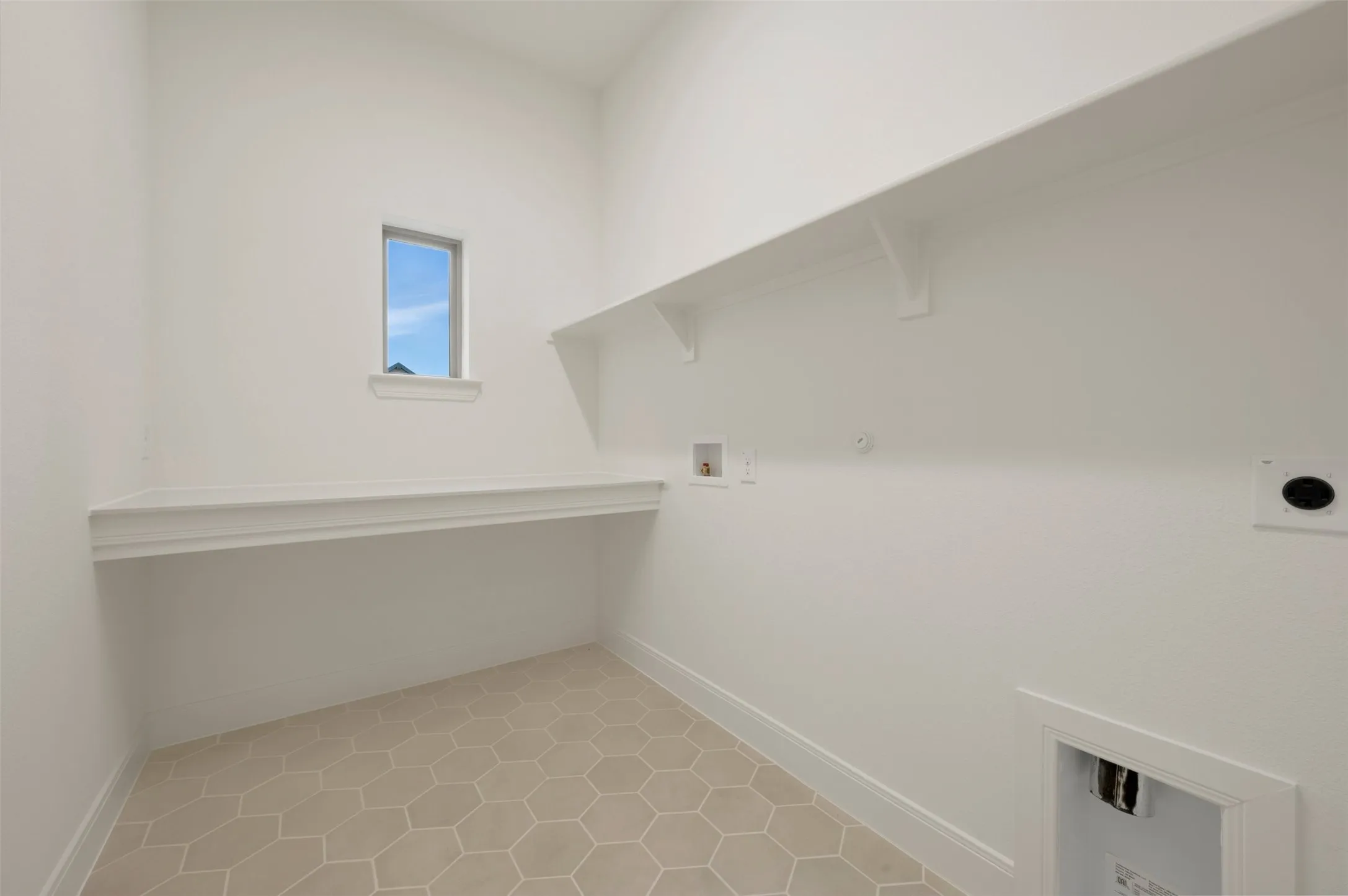 Laundry area featuring hexagon tile flooring, a built-in folding counter, and overhead shelving